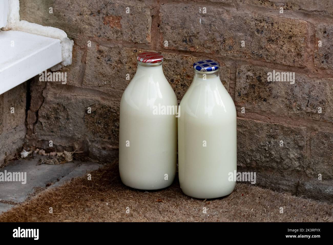 Two pints of milk in glass bottles on a doorstep in Yorkshire, England. The red top is semi-skimmed milk, the blue top is skimmed. Stock Photo