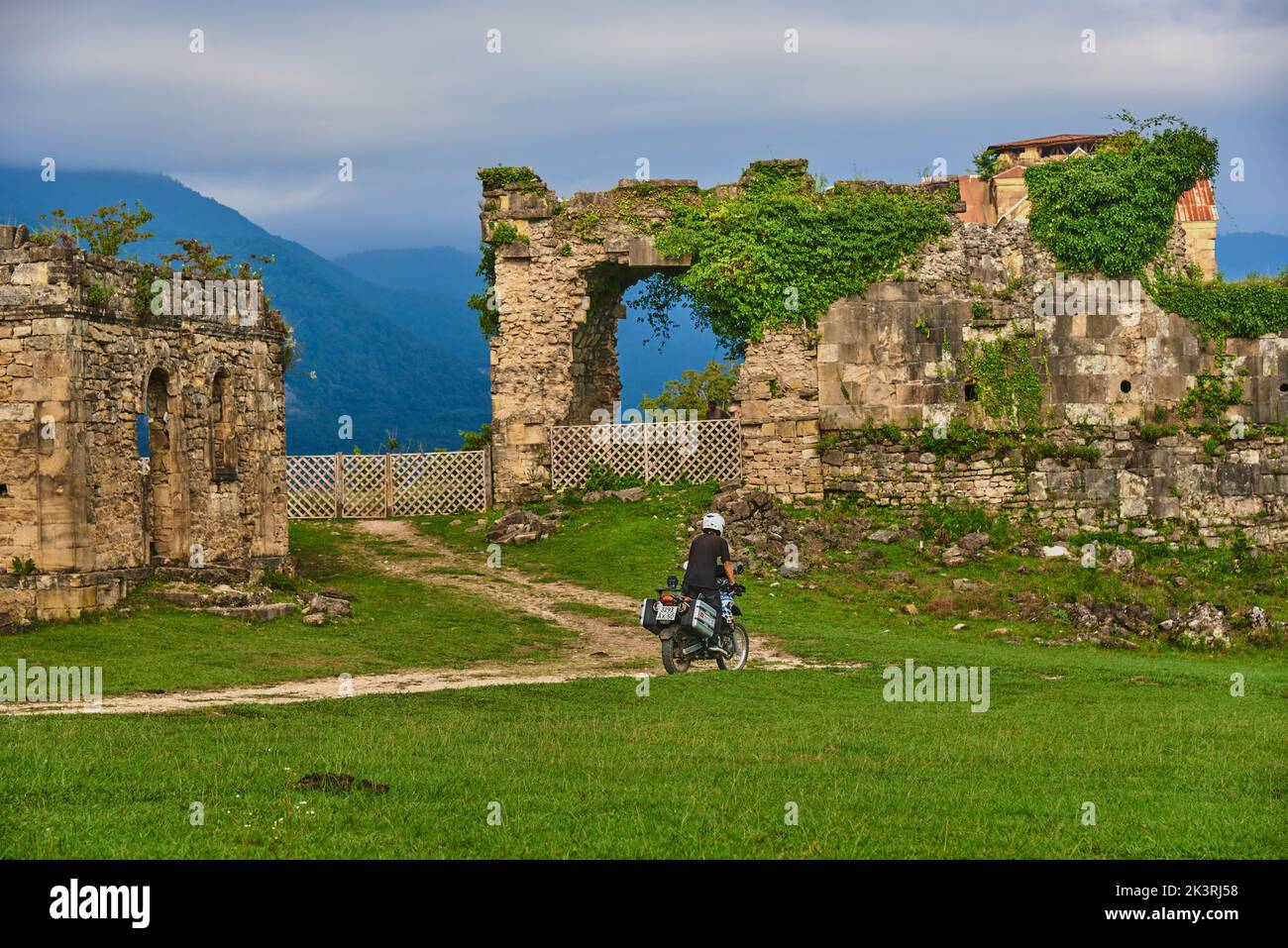 Abkhazia, the village of Agubedia, the Bedia Cathedral, August 2022. A man on a motorcycle rides along a dirt road among green grass to the ruins of a Stock Photo