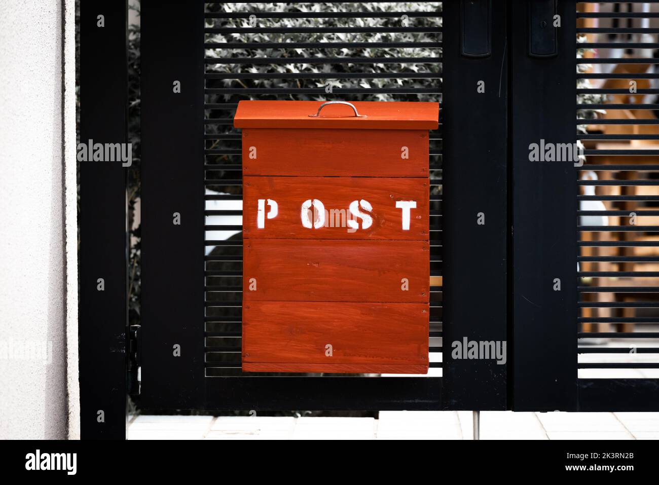 A red wooden post mail box at the entrance gate of a house. Stock Photo