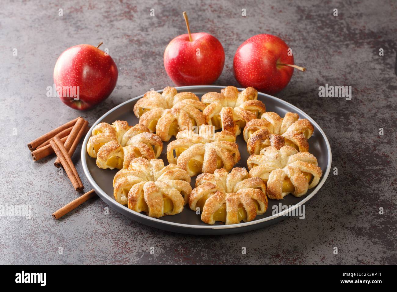 Dessert flower Apple rings in puff pastry with sugar and cinnamon close-up in a plate on the table. Horizontal Stock Photo
