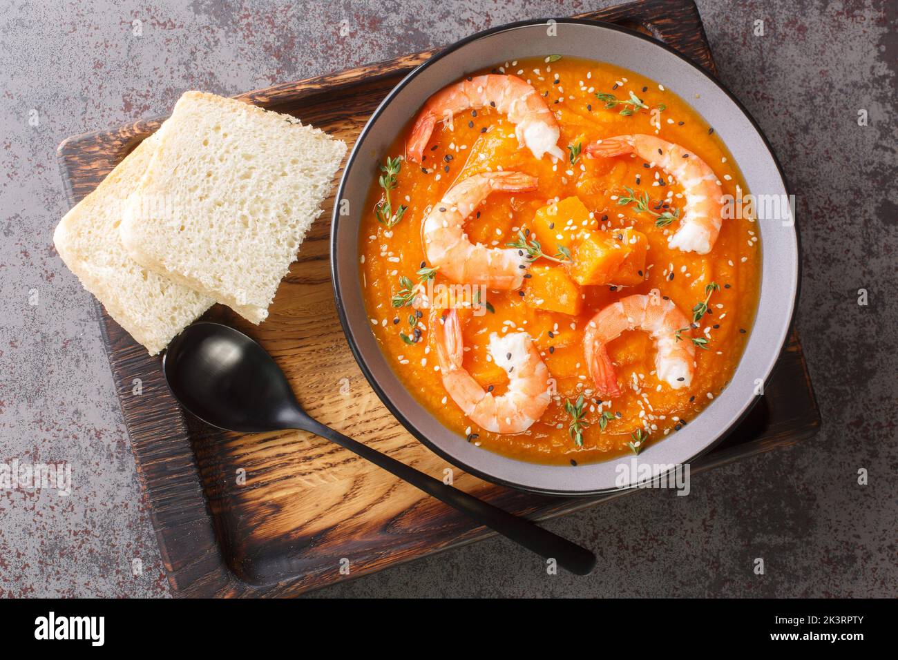 Pumpkin vegetable soup with shrimps, sesame seeds and thyme close-up on a wooden tray on the table. Horizontal top view from above Stock Photo