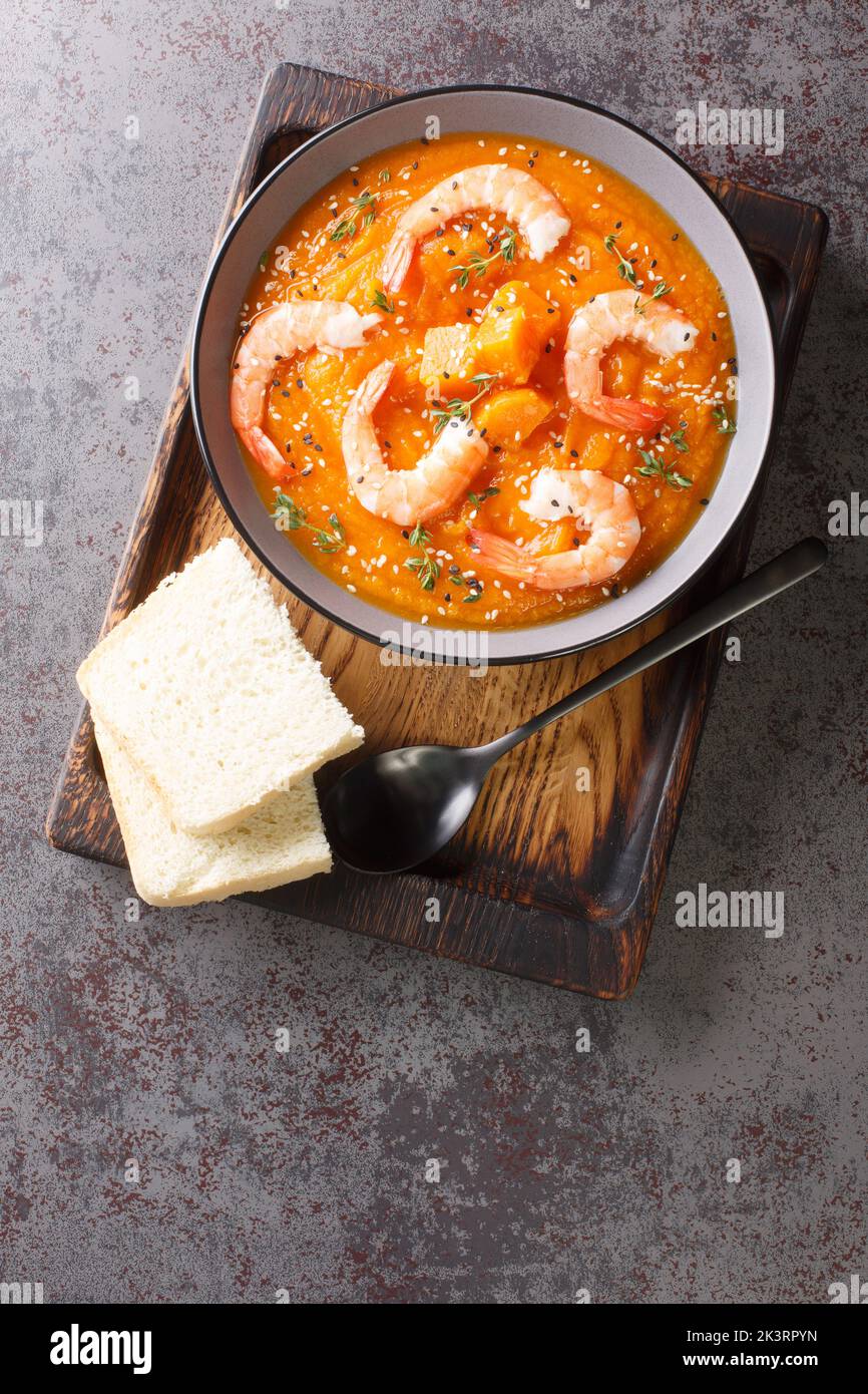 Pumpkin puree soup with shrimp, sesame and thyme served with bread on a wooden tray on the table. Vertical top view from above Stock Photo