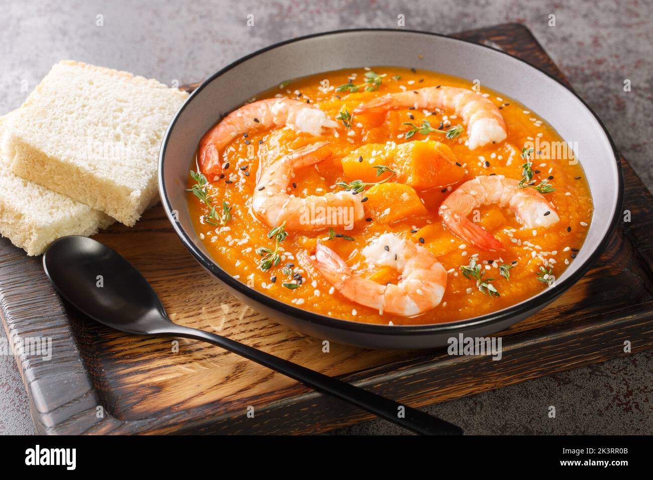 Pumpkin vegetable soup with shrimps, sesame seeds and thyme close-up on a wooden tray on the table. Horizontal Stock Photo