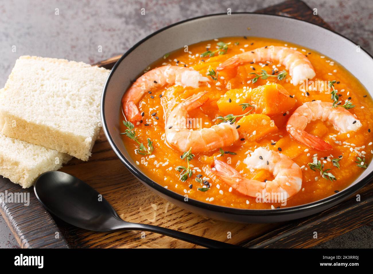 Thick autumn pumpkin soup with shrimp, sesame and thyme served with bread on a wooden tray on the table. Horizontal Stock Photo