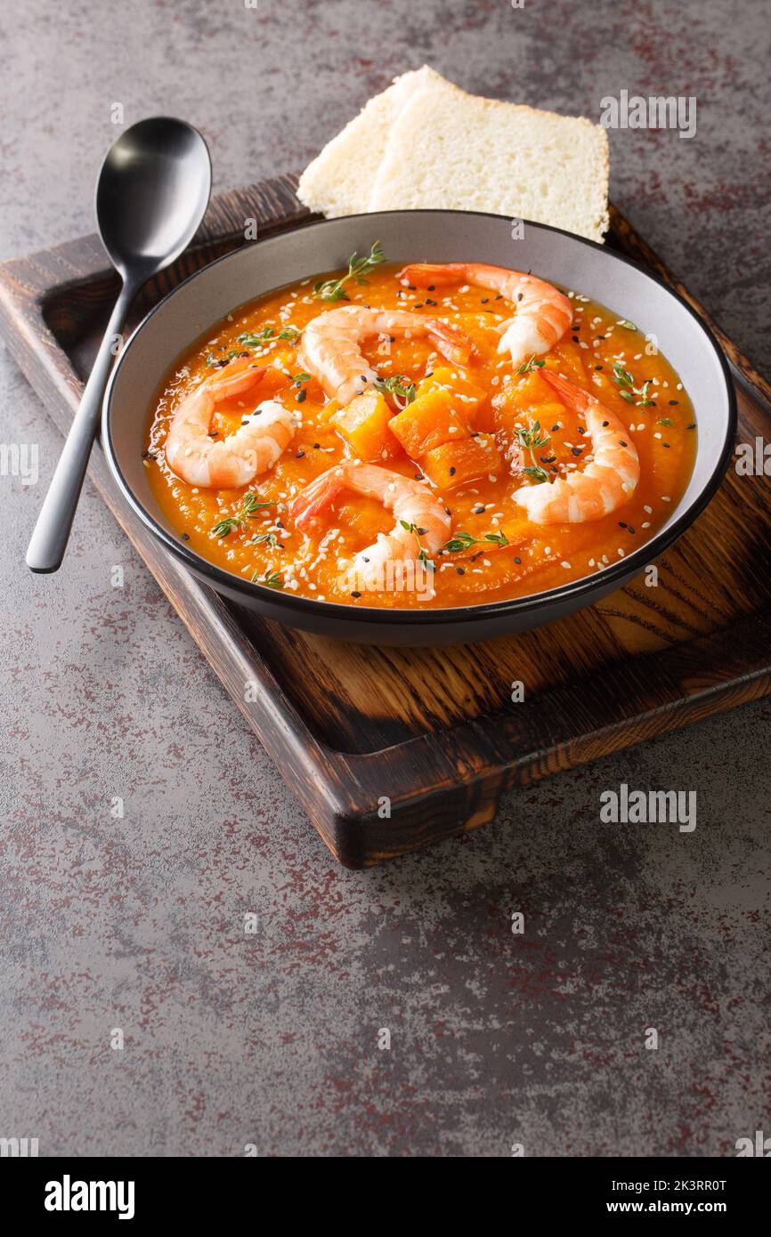 Pumpkin puree soup with shrimp, sesame and thyme served with bread on a wooden tray on the table. Vertical Stock Photo