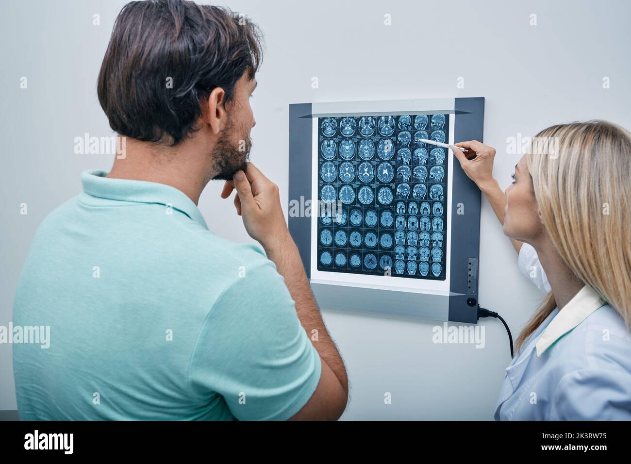 Practicing doctor together with male patient watching MRI scan of brain on negatoscope in doctor's office. CT scan, MRI of head, radiology result Stock Photo