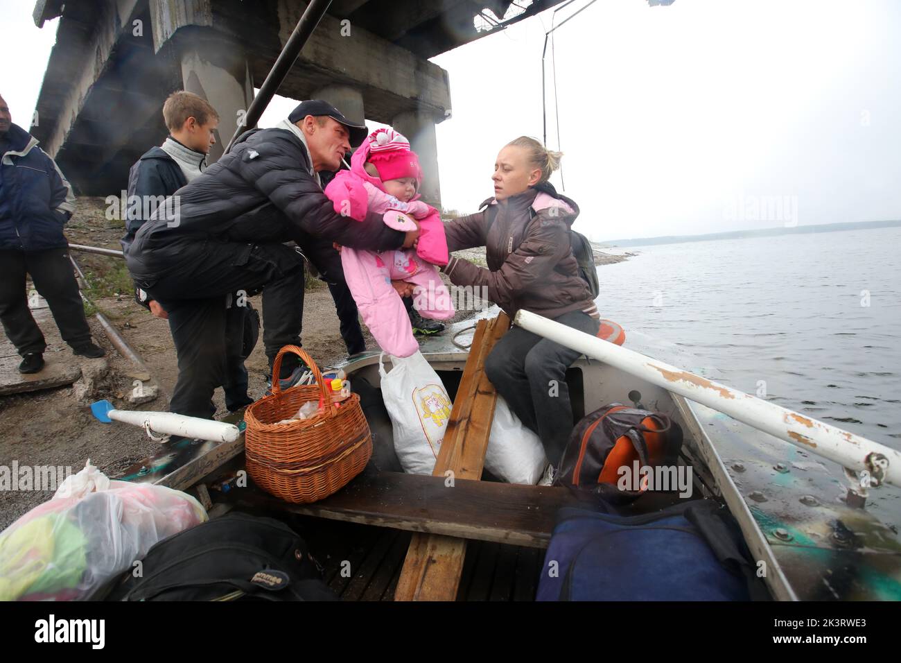 KHARKIV REGION, UKRAINE - SEPTEMBER 27, 2022 - A man passes a baby girl to a woman as Staryi Saltiv residents use a boat to get across the Pechenihy R Stock Photo