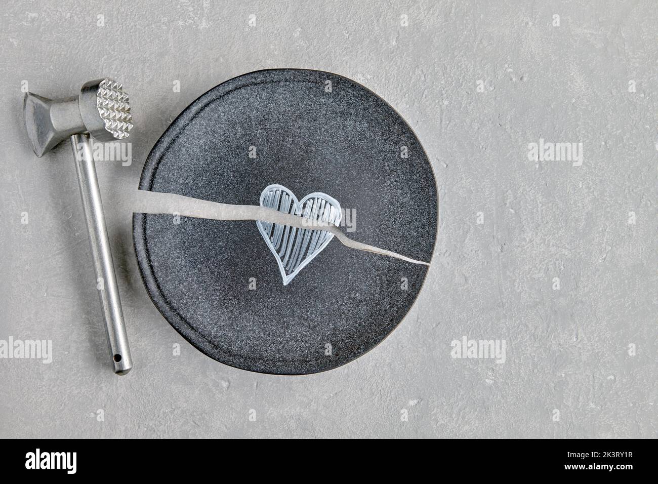 Broken ceramic plate with a painted heart and a kitchen hammer o Stock Photo
