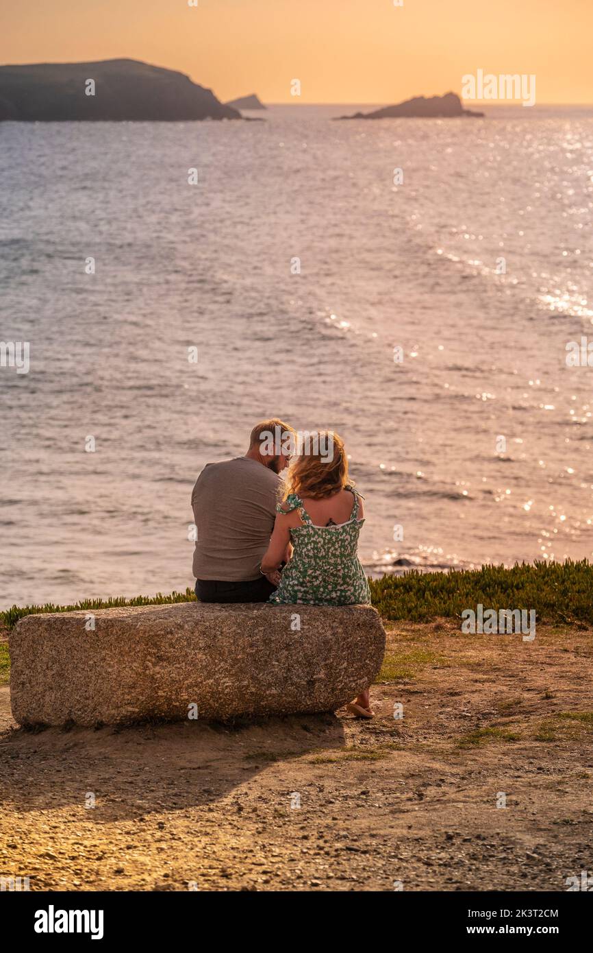 A couple sitting closely together on a rock on the coast overlooking Fistral Bay in Newquay in Cornwall in the UK in Europe Stock Photo
