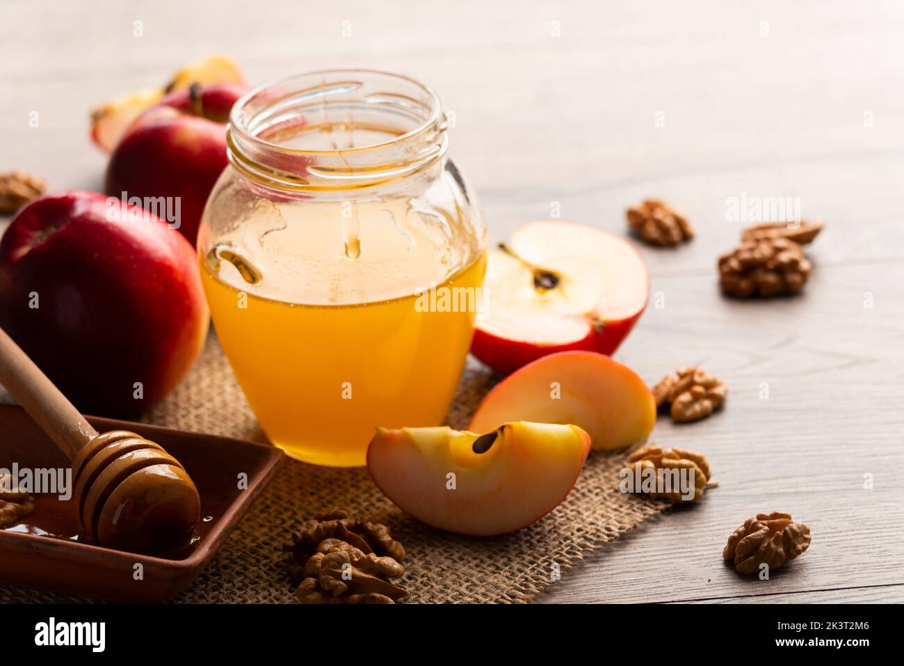 Mason jar with honey honey dipper red apples and walnuts on kitchen table Stock Photo