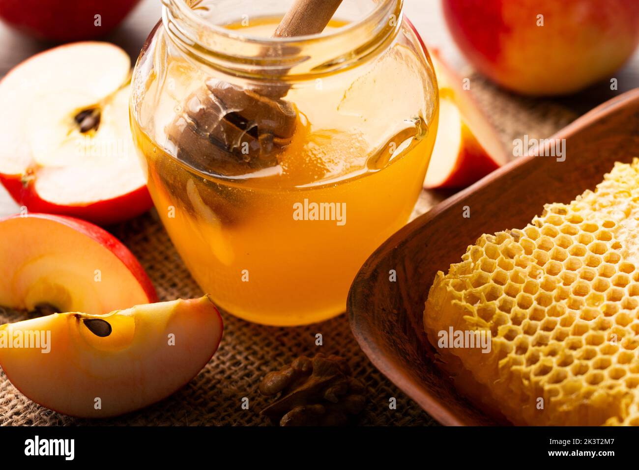 Mason jar with honey honey dipper and red apples and honeycomb on kitchen table Stock Photo