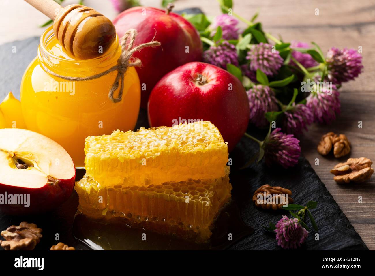 Mason jar with honey, honey dipper, honeycomb, red apples and walnuts on kitchen table Stock Photo