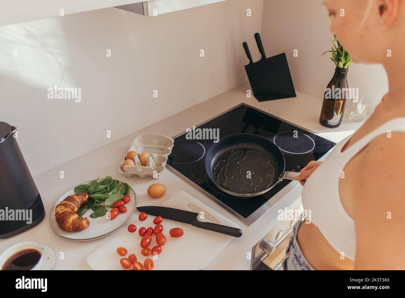 Cropped view of woman in top holding frying pan near cherry tomatoes and eggs in kitchen,stock image Stock Photo