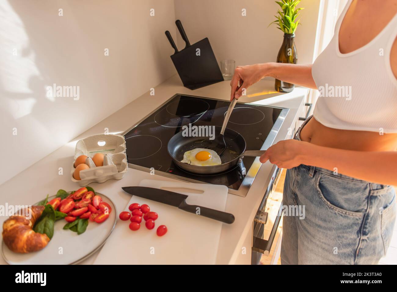 Cropped view of woman in top frying egg near cherry tomatoes and croissant in kitchen,stock image Stock Photo