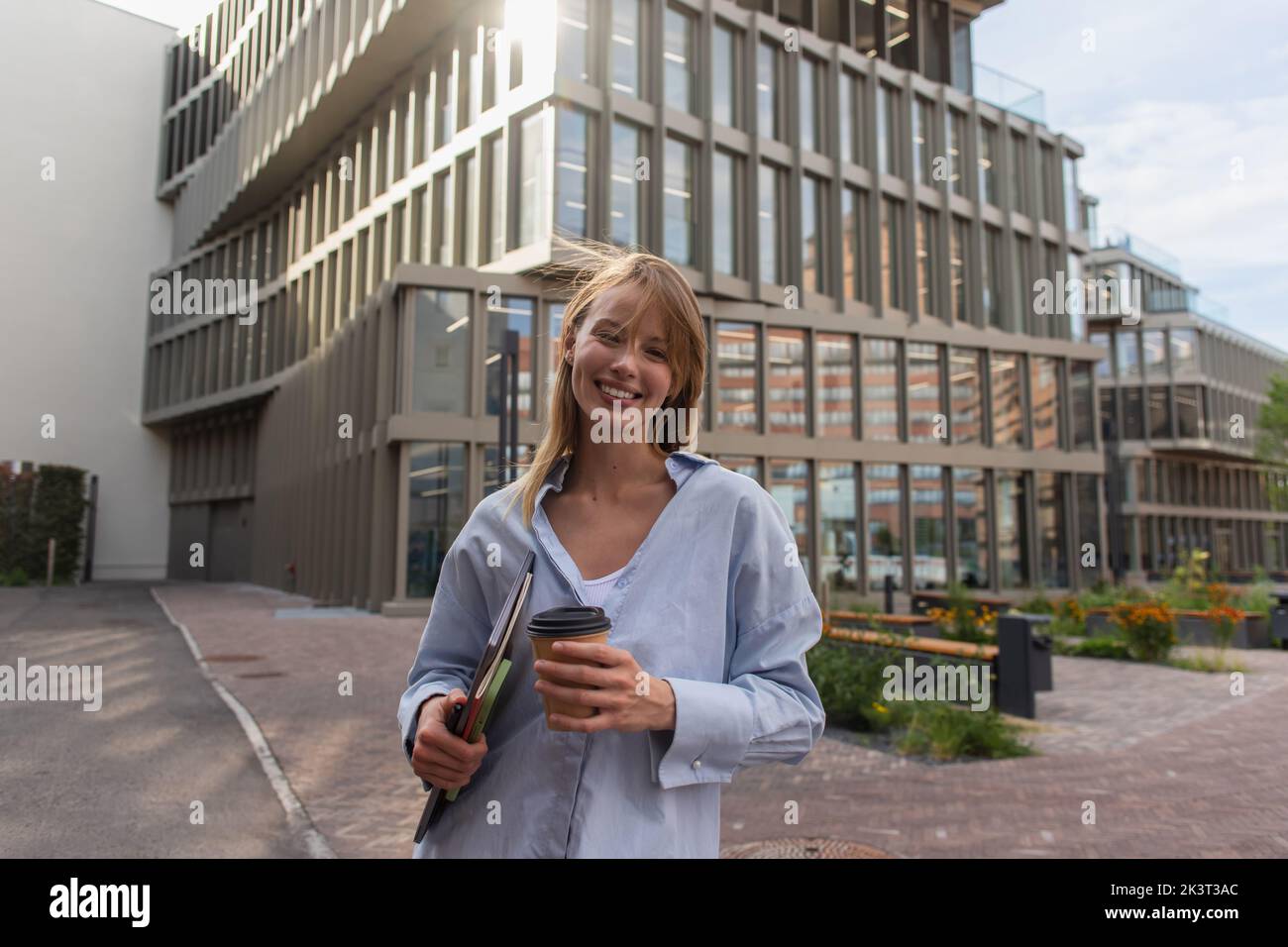 Positive blonde woman holding devices and coffee to go on urban street in Berlin,stock image Stock Photo