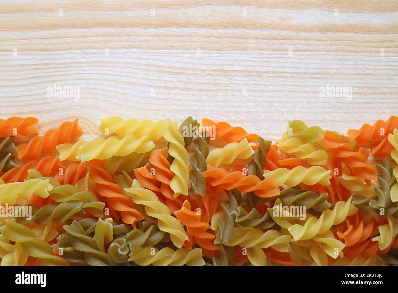 Heap of Vegeroni spiral shaped three-color fusilli pasta on wooden background Stock Photo