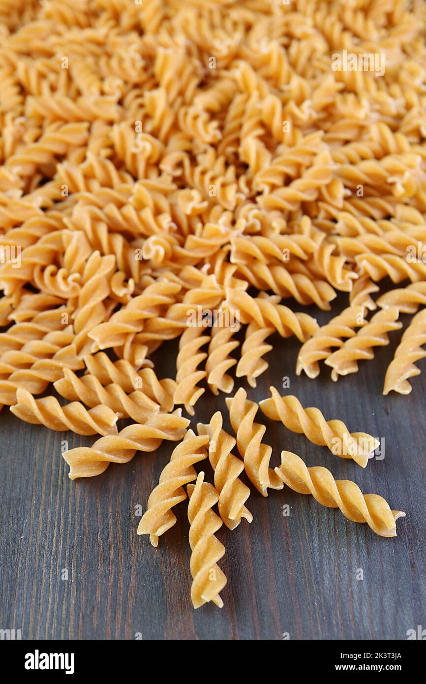 Pile of Uncooked Whole Wheat Fusilli Pasta Scattered on Black Wooden Background Stock Photo