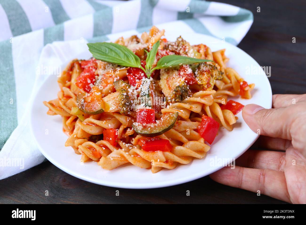 Hand Placing a Plate of Delectable Fusilli Pasta in Marinara Sauce on Wooden Table Stock Photo