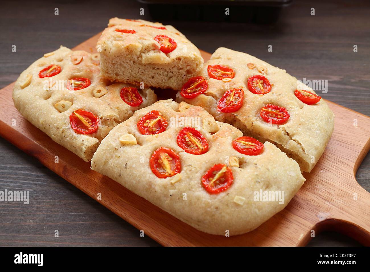 Mouthwatering Homemade Tomato and Garlic Italian Focaccia Bread on Wooden Breadboard Stock Photo
