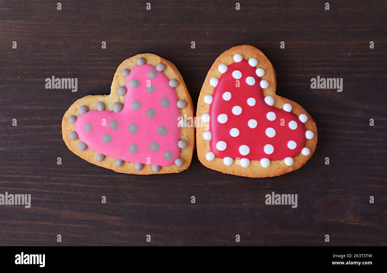 Pair of dotted heart shaped royal icing cookies on black wooden background Stock Photo