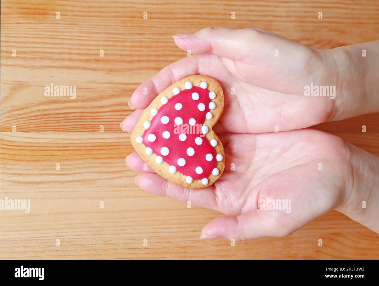 Red and white heart shaped royal icing cookie in woman's hand on wooden background Stock Photo