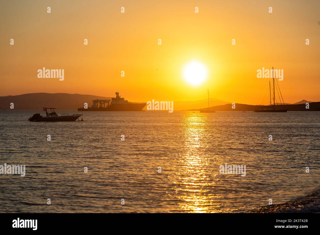 Naxos island, sunset over colorful Aegean sea, Cyclades destination Greece. Sundown with orange and gold yellow beams colors sky background and boats Stock Photo