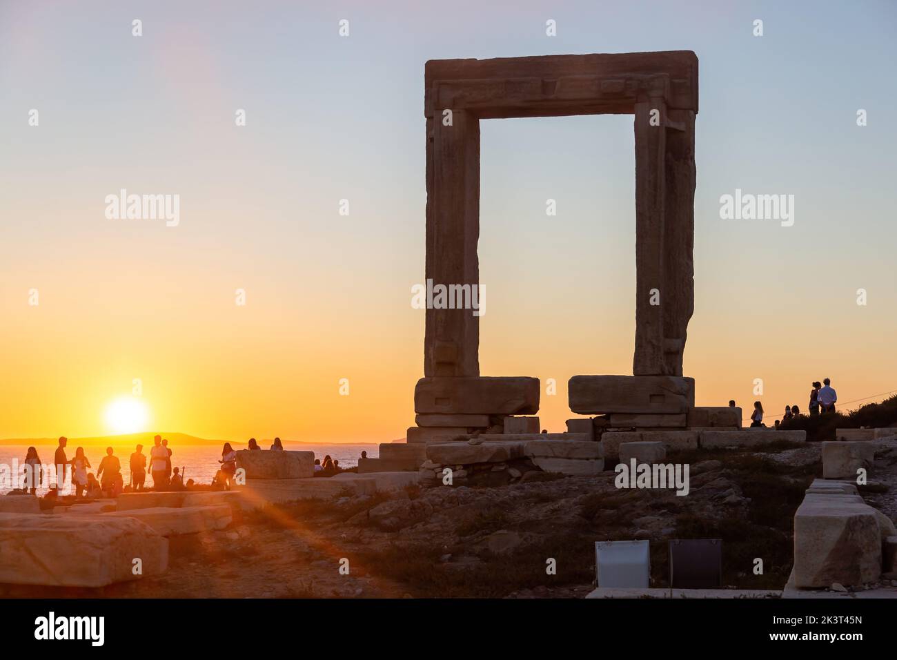Naxos island, sunset over Temple of Apollo, Cyclades Greece. People admires the sundown from the islet of Palatia. Sunbeams paint the sky background. Stock Photo