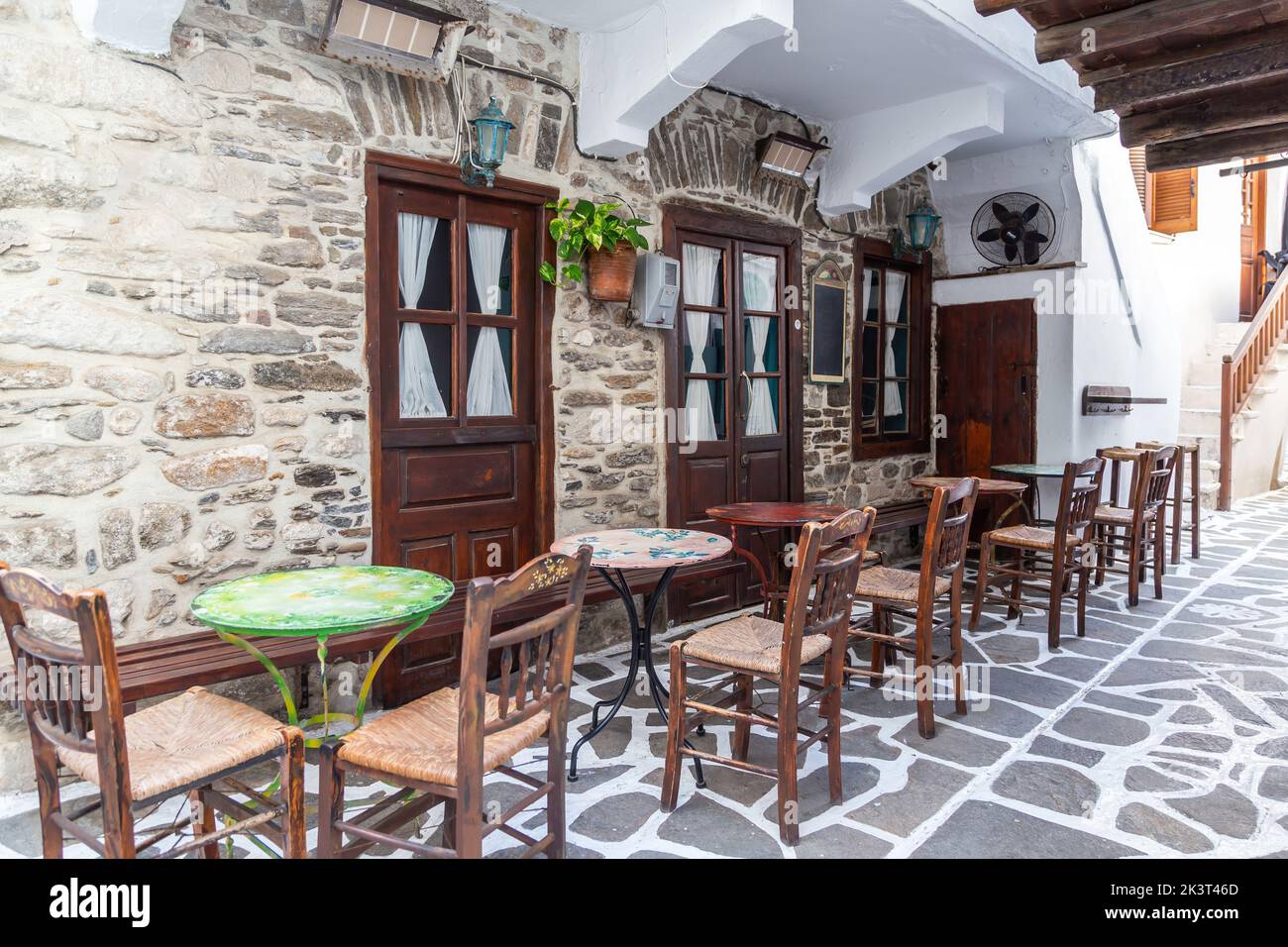 Naxos island, Cyclades Greece. Traditional outdoors empty cafe with wooden bench ornate chair and table on cobblestone street. Summer holiday destinat Stock Photo