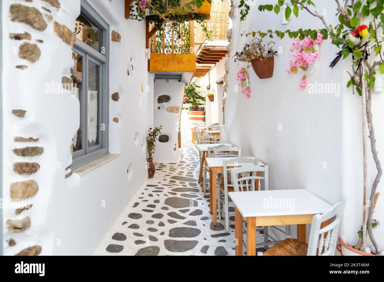 Naxos island, Cyclades Greece. Traditional outdoors cafe, wooden chair and table on cobblestone street. Whitewashed wall, plants around. Summer holida Stock Photo