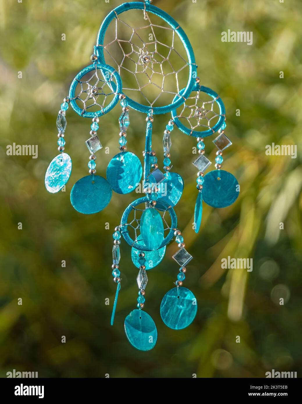 A blue dream catcher hangs against a blurred green background Stock
