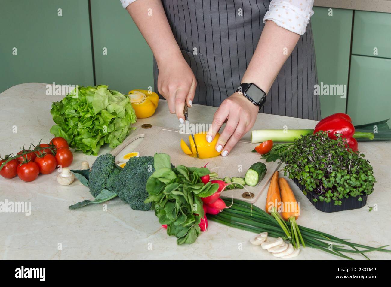 Woman is preparing vegetable salad in the kitchen and cutting ingredients on the table. Healthy Vegan Food.  Stock Photo