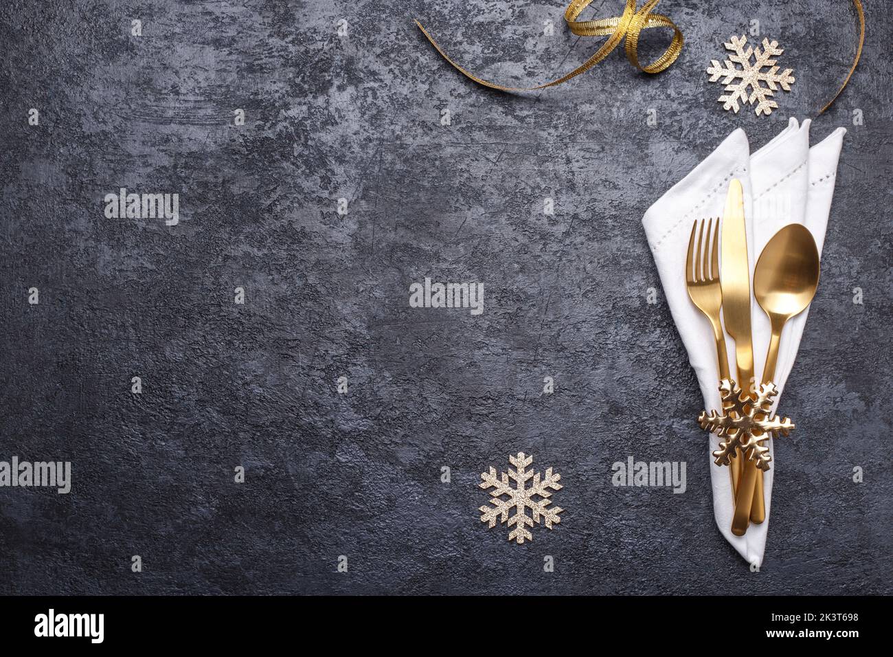 Table setting with golden cutlery and white napkin on the black stone table, Christmas or new year card or menu template copy space flat lay Stock Photo