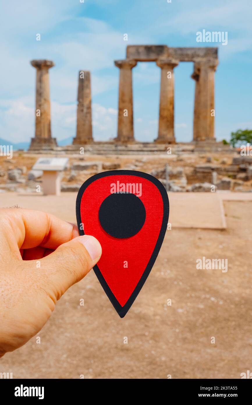 closeup of the hand of a man holding a red marker pointing the remains of the famous Temple of Apollo, in the Ancient Corinth Greece Stock Photo