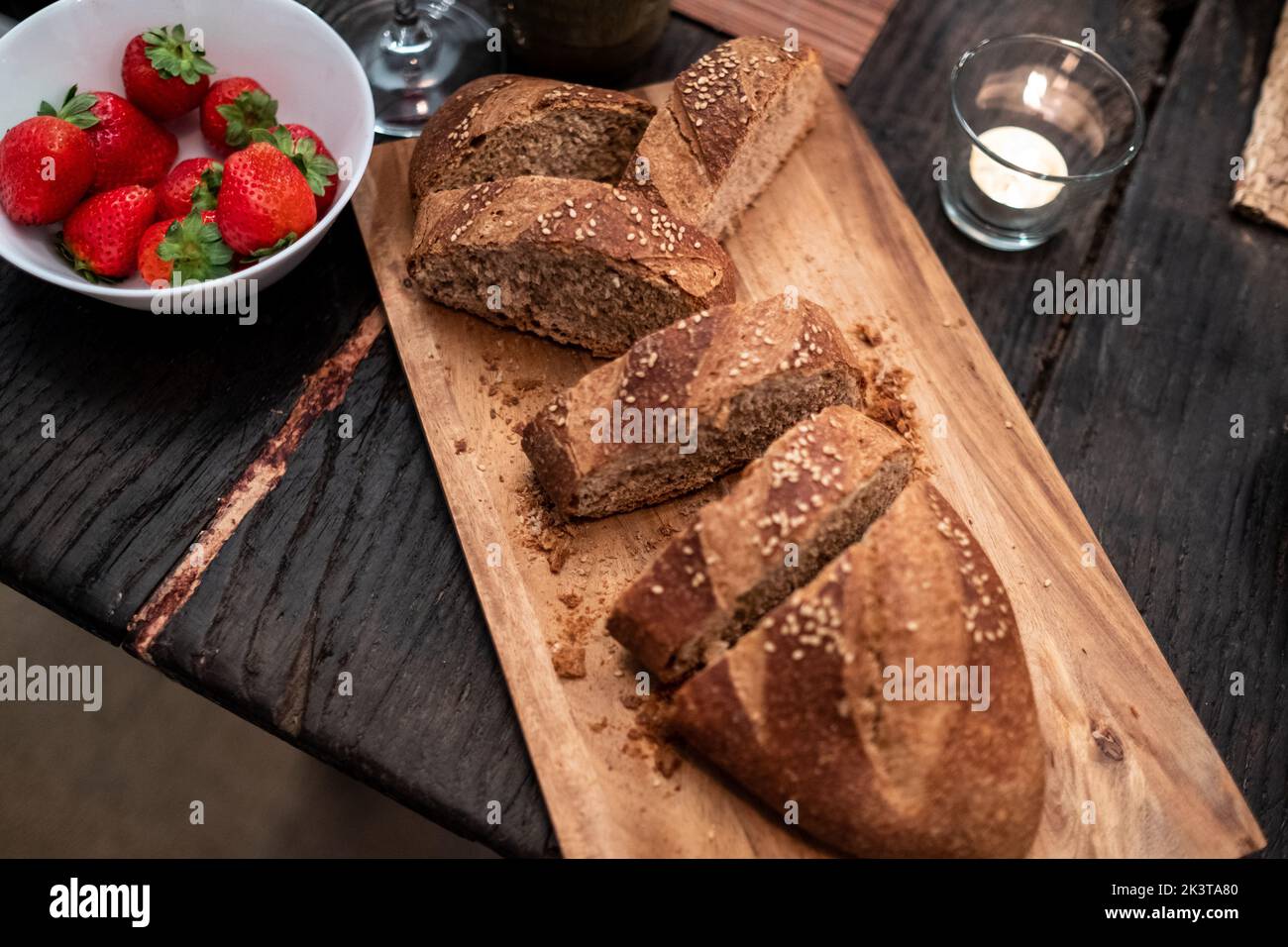From above tasty cut crispy wholegrain fresh bread on wooden board and fresh strawberry in bowl on table Stock Photo