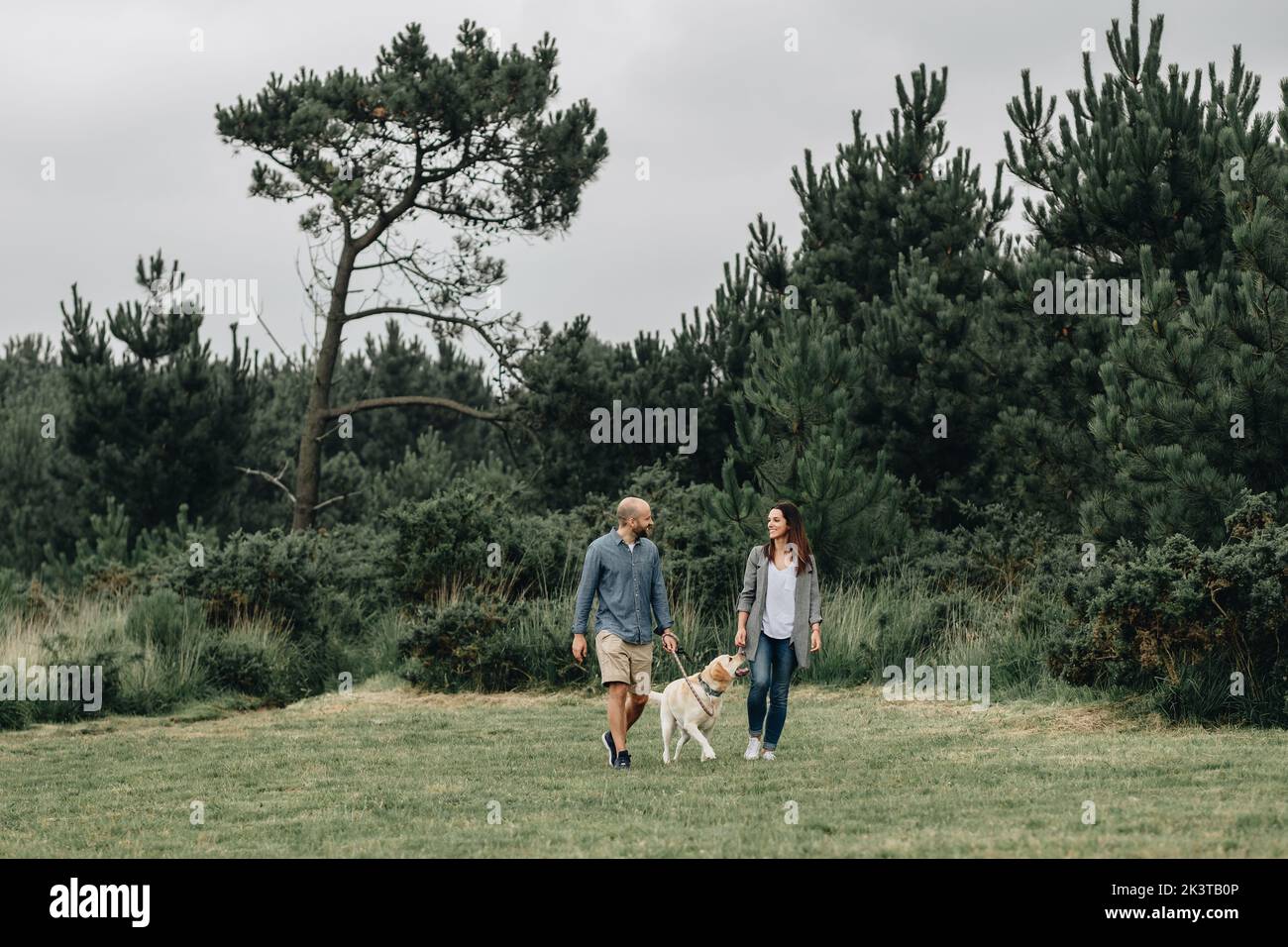 Happy couple in casual wear walking with dog in green park Stock Photo ...