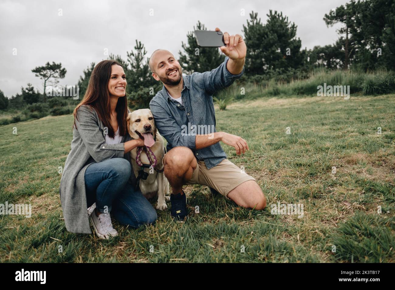 Lovely couple hugging Labrador Retriever and having fun taking selfie ...