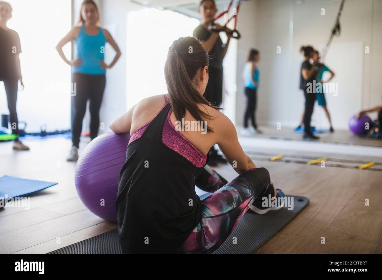 Side view of young female sitting on mat and exercising with fit ball ...