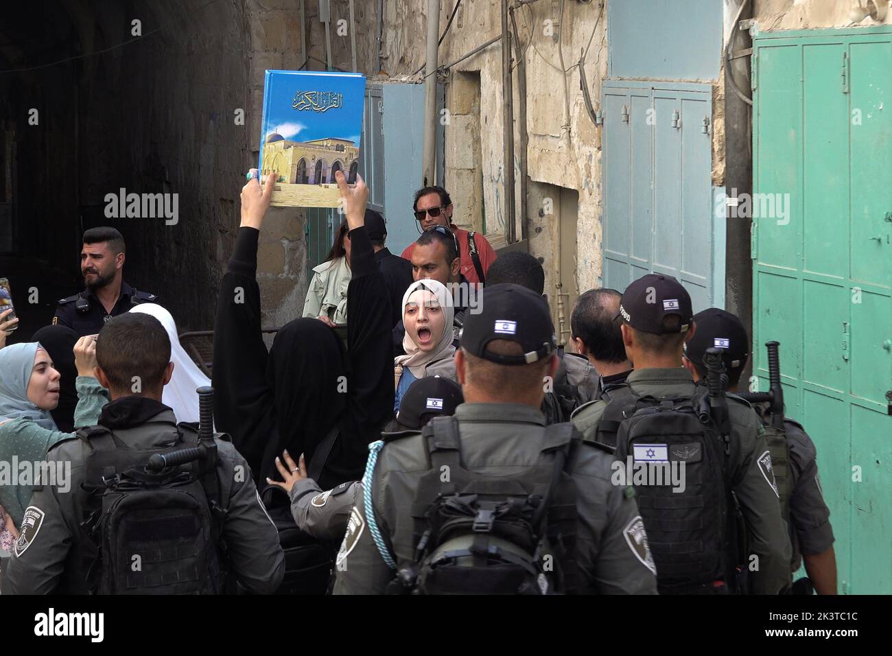 A Palestinian woman holds up a book bearing the photo of al-Aqsa Mosque compound as members of the Israeli Security Forces push back Palestinian women protesting the visit of religious Jews in the Temple Mount in Chain Gate street in the old city on September 27, 2022 in Jerusalem, Israel. Stock Photo