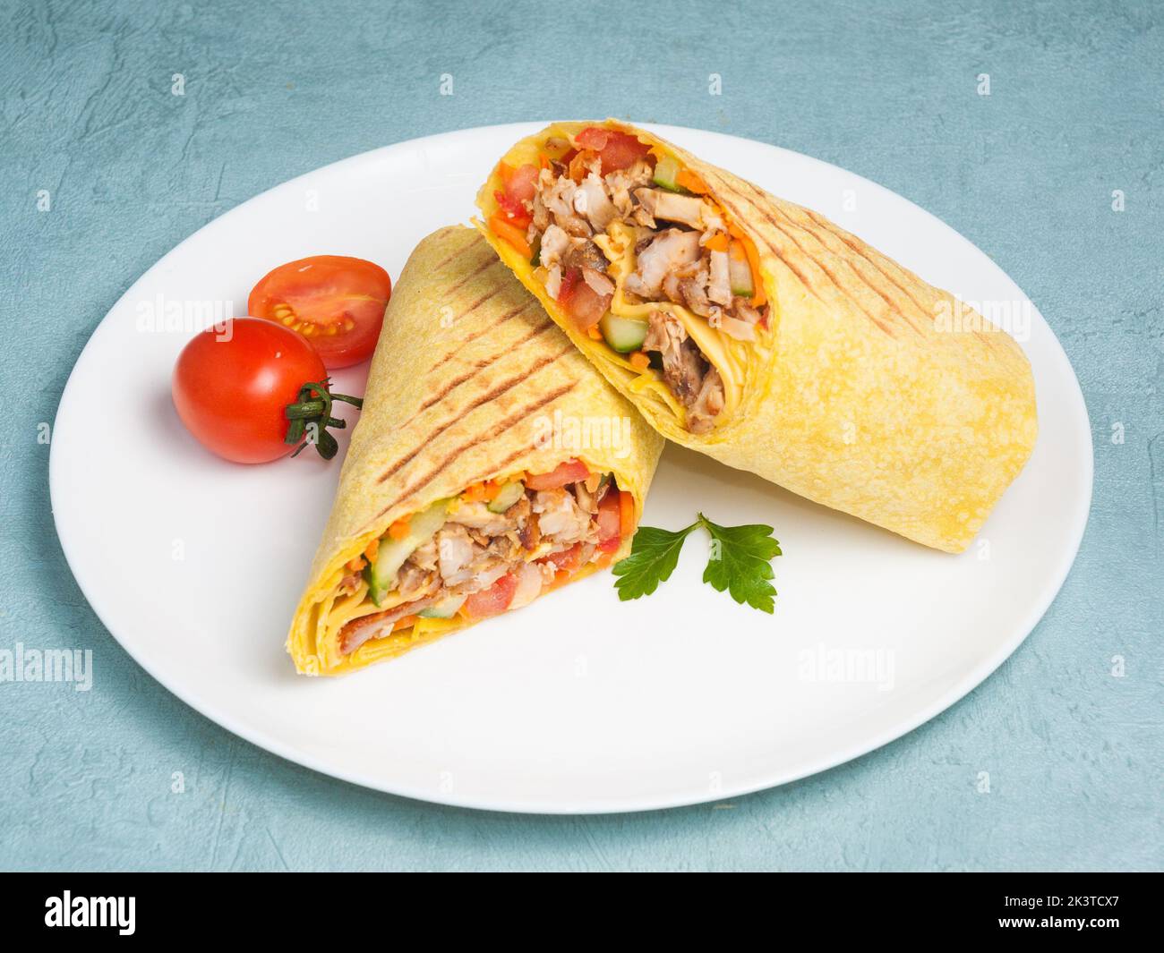 tasty shawarma with chicken and vegetables in cheese pita bread on a blue background Stock Photo