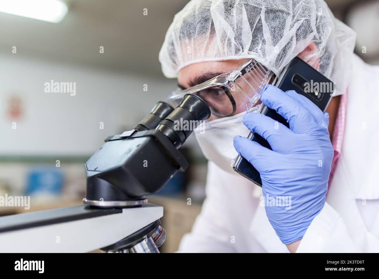 Man working at a lab using a smartphone while using a microscope at a laboratory Stock Photo