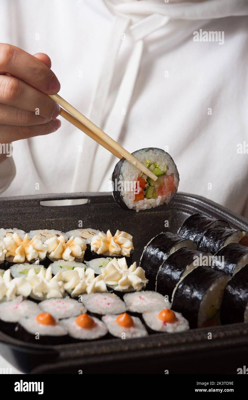 a girl in light clothes eats tasty rolls from a container Stock Photo