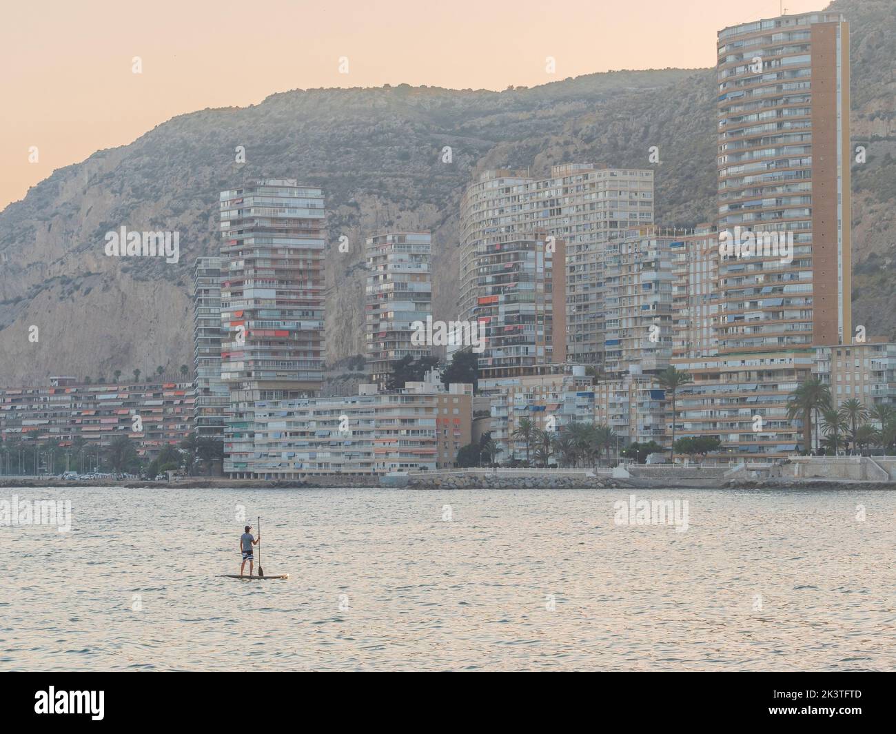 Back view of unrecognizable sporty man swimming on surfboard paddle looking at amazing cityscape in Alicante Spain Stock Photo