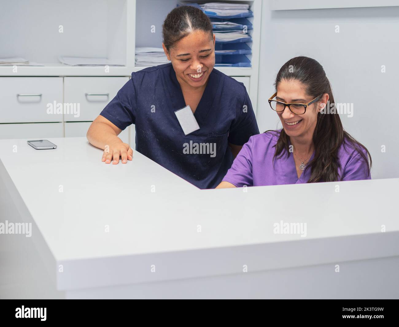 Female nurses in scrubs smiling while working behind counter on