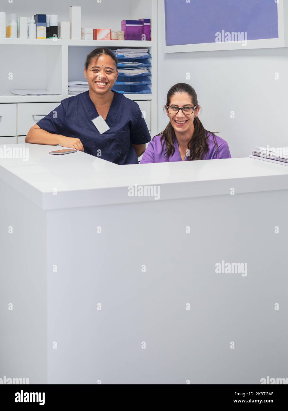 Female nurses in scrubs smiling while working behind counter on