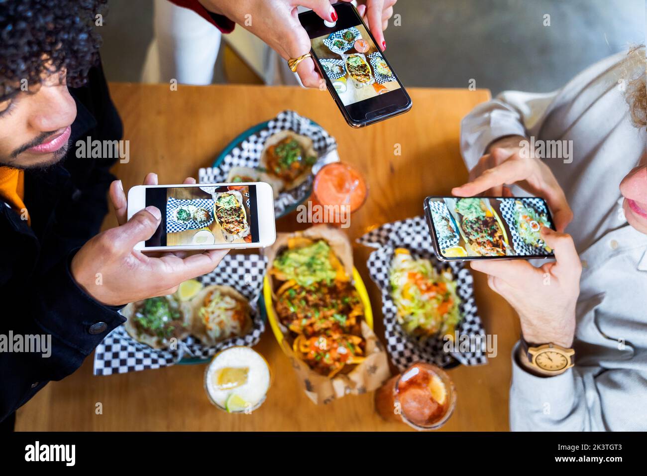 Top view crop anonymous friends taking pictures of delicious food on smartphones while gathering at table in restaurant Stock Photo
