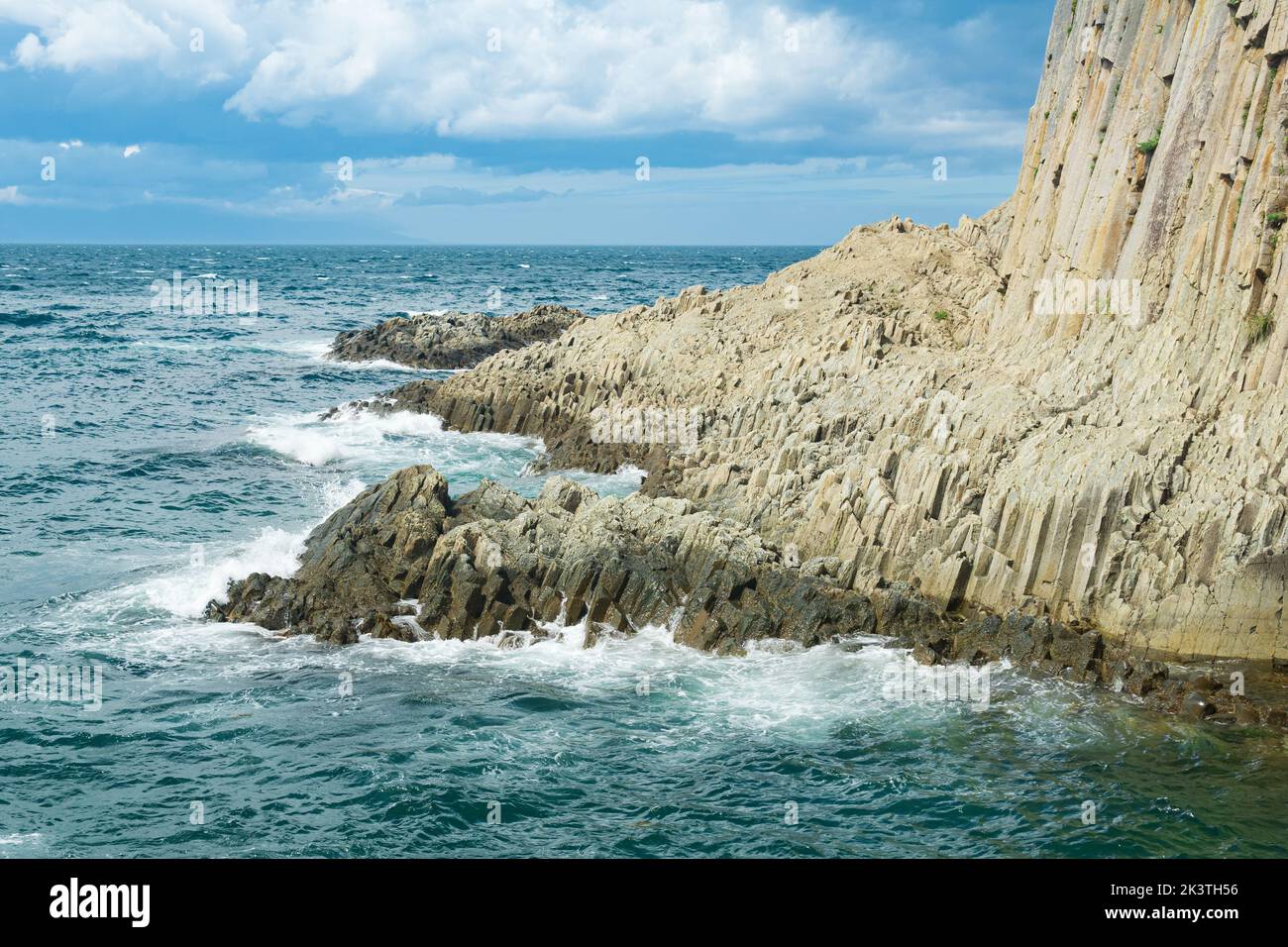 rocky seashore formed by columnar basalt against the backdrop of a sea, coastal landscape of the Kuril Islands Stock Photo
