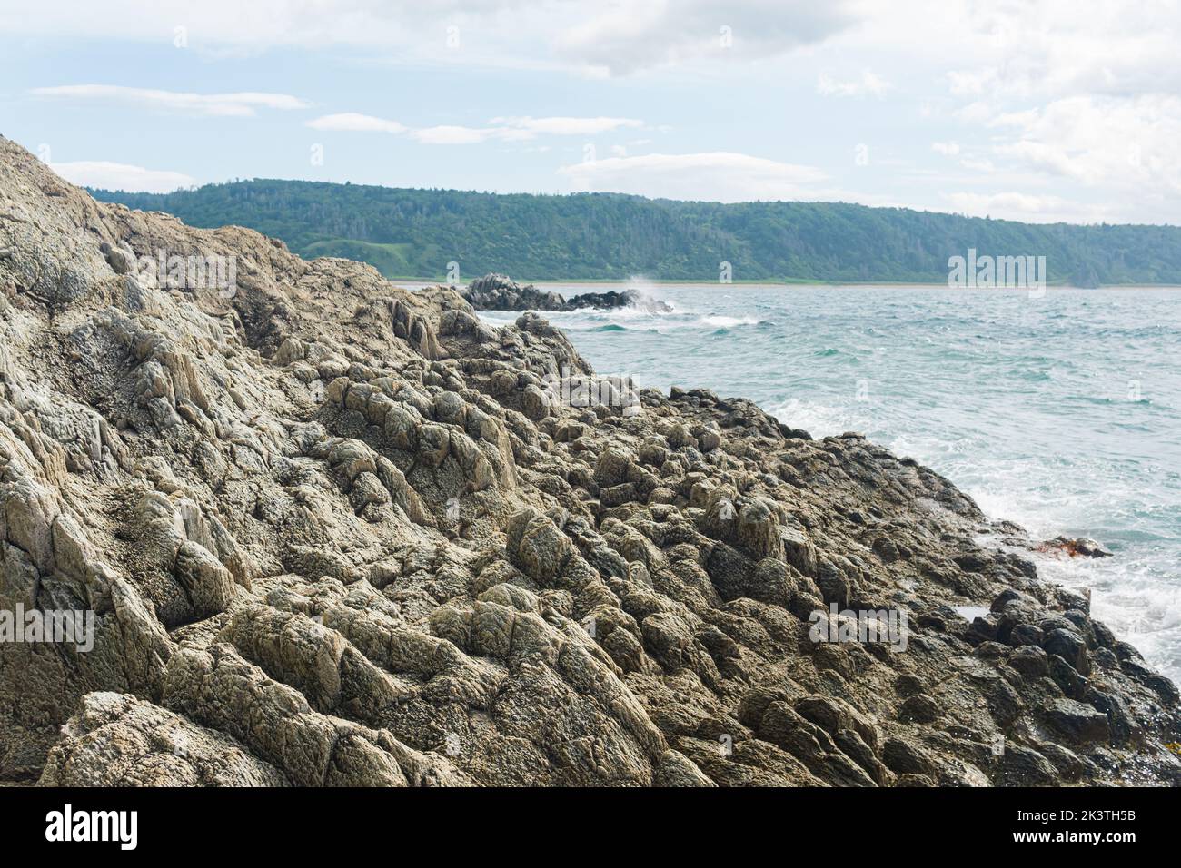 coastal cliff formed by solidified lava close-up against the background of a distant sea shore Stock Photo