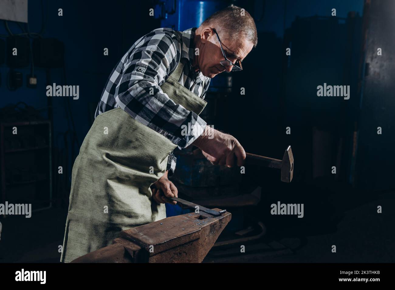 Senior an artisan blacksmith knocks with a hammer on iron to shape. Stock Photo