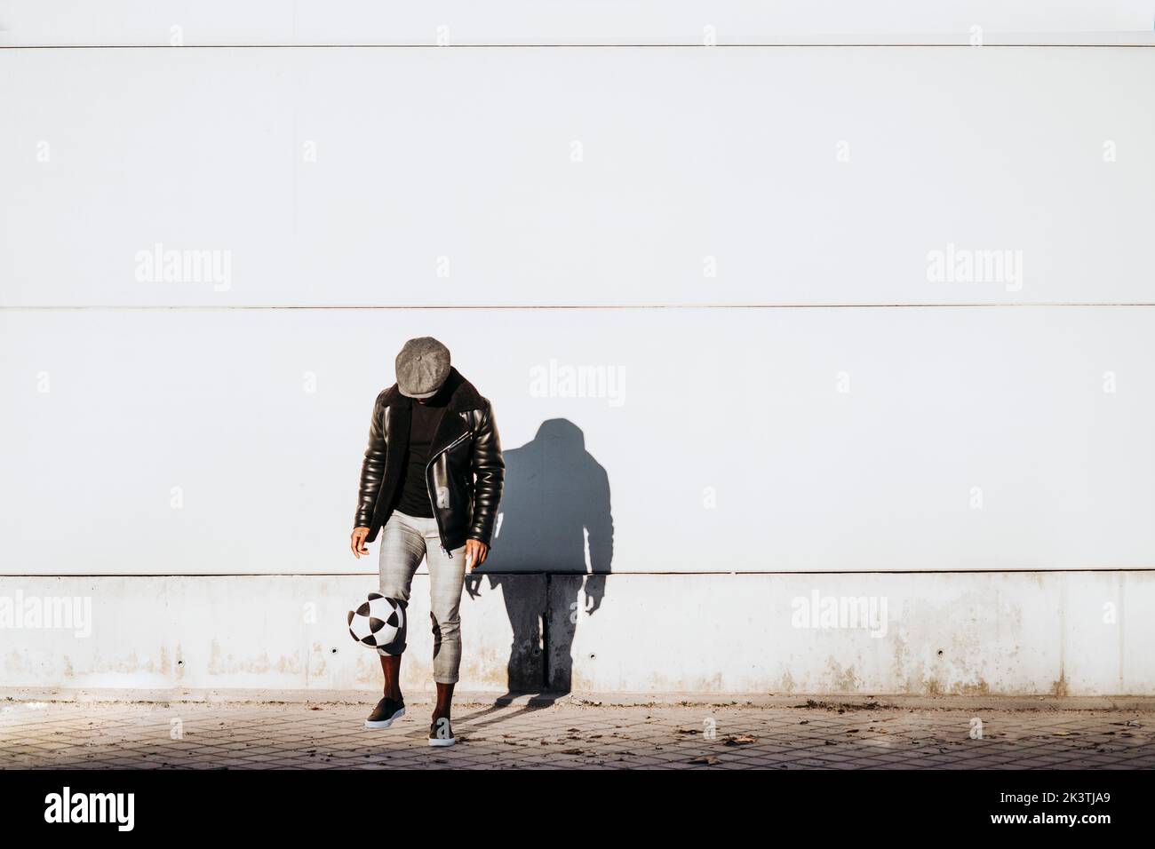 Black man kicking ball on street on white wall Stock Photo Alamy