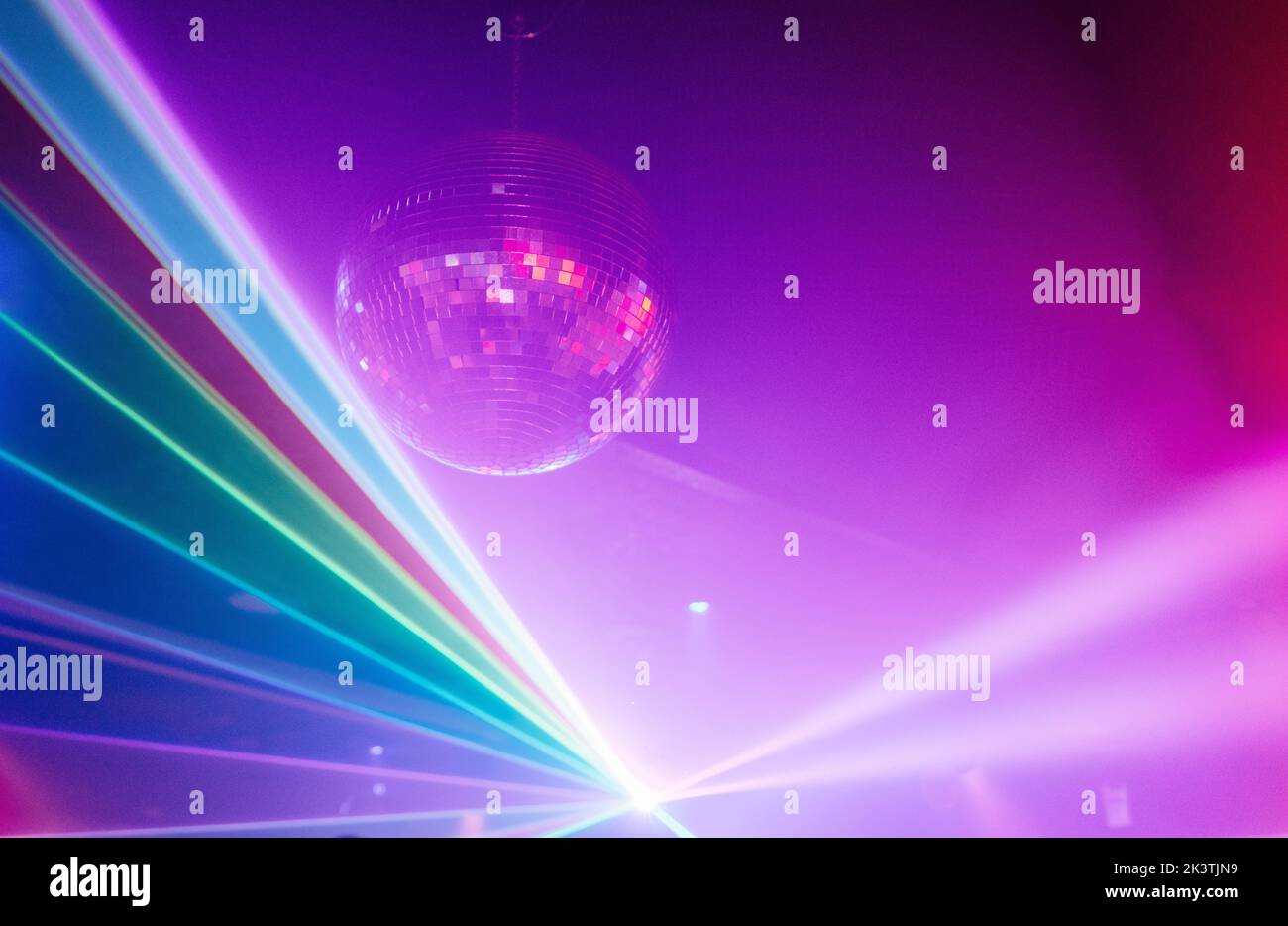Modern disco ball shining under red neon light on ceiling of